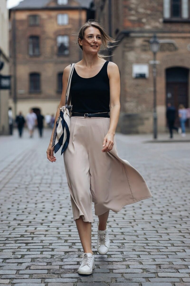 Woman in a white crewneck tee and beige linen tie-waist shorts with beige espadrille platform shoes and an off-white canvas tote in a hallway mirror selfie.