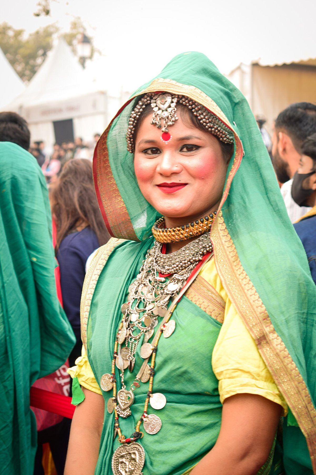 Woman wearing an emerald green traditional outfit with a mint green dupatta over her head, layered silver necklaces, a maang tikka and a red bindi