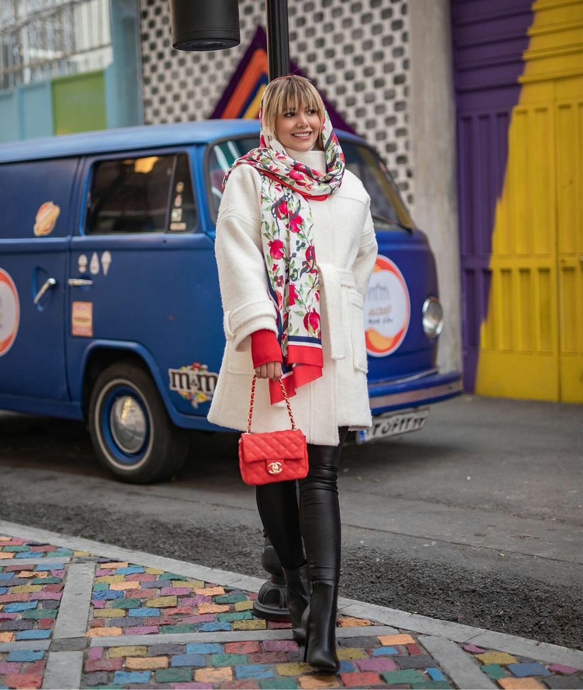 woman wearing a cream wool coat, floral scarf, black heeled knee boots and black leggings on a city street