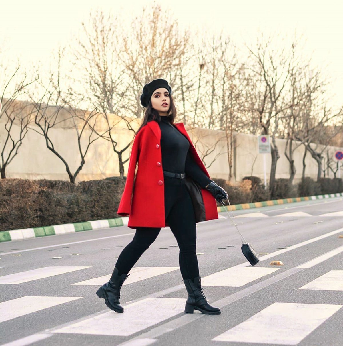 Woman in a bright red coat, black turtleneck, black trousers and lace-up boots with a black beret, crossing a city street
