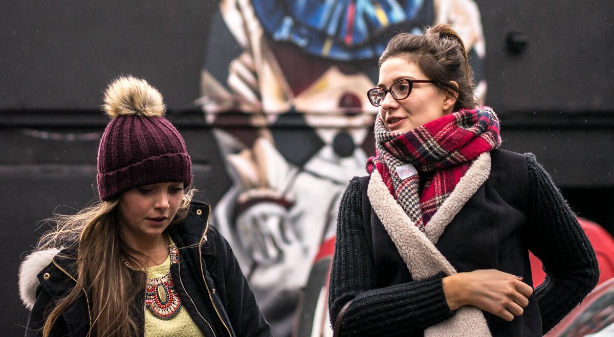 Street-style photo of a young woman in Dublin wearing a red and black tartan scarf wrapped over a dark cardigan