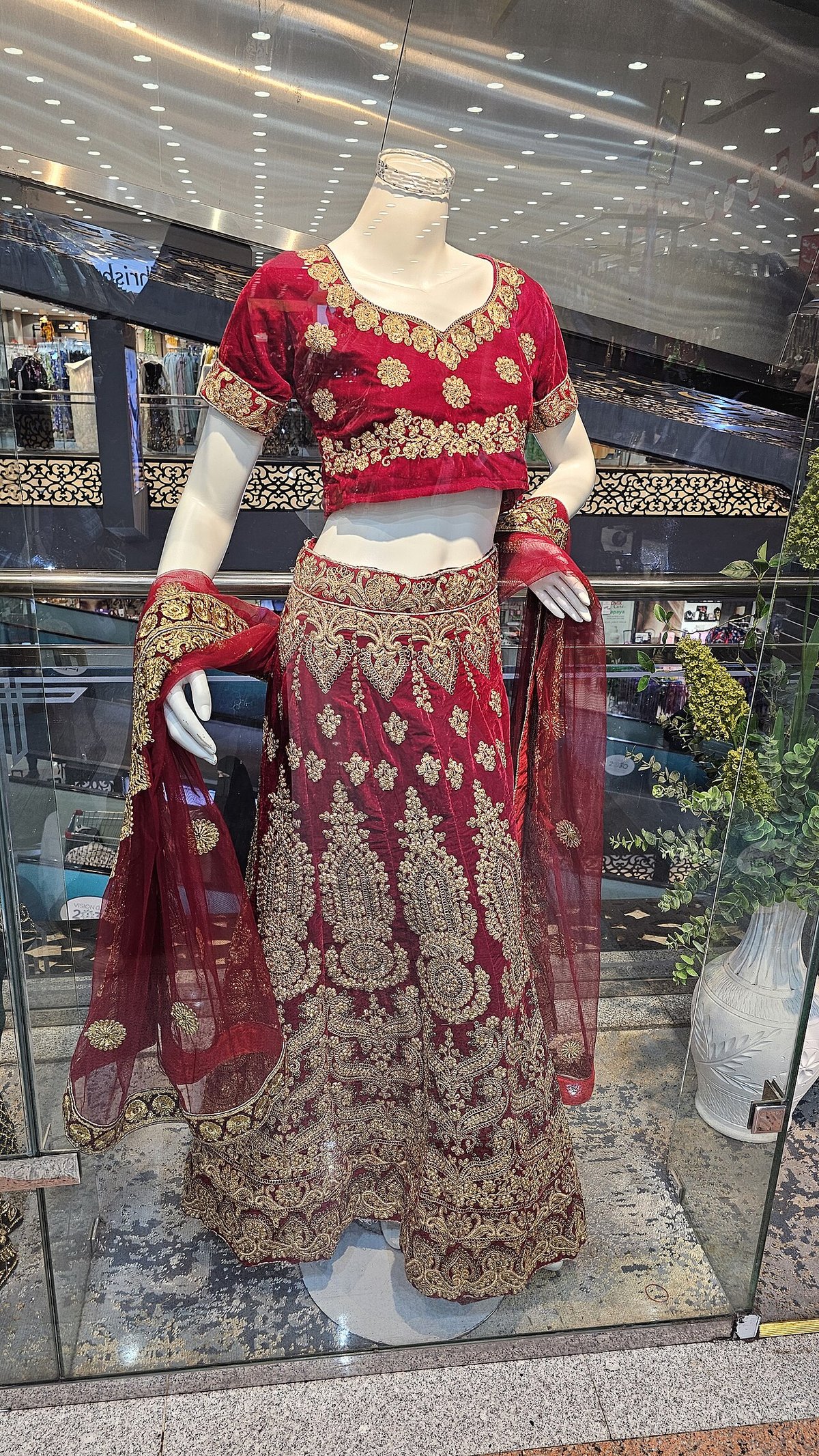 Shop mannequin wearing a red velvet choli and a red lehenga skirt with heavy gold embroidery and a sheer red dupatta