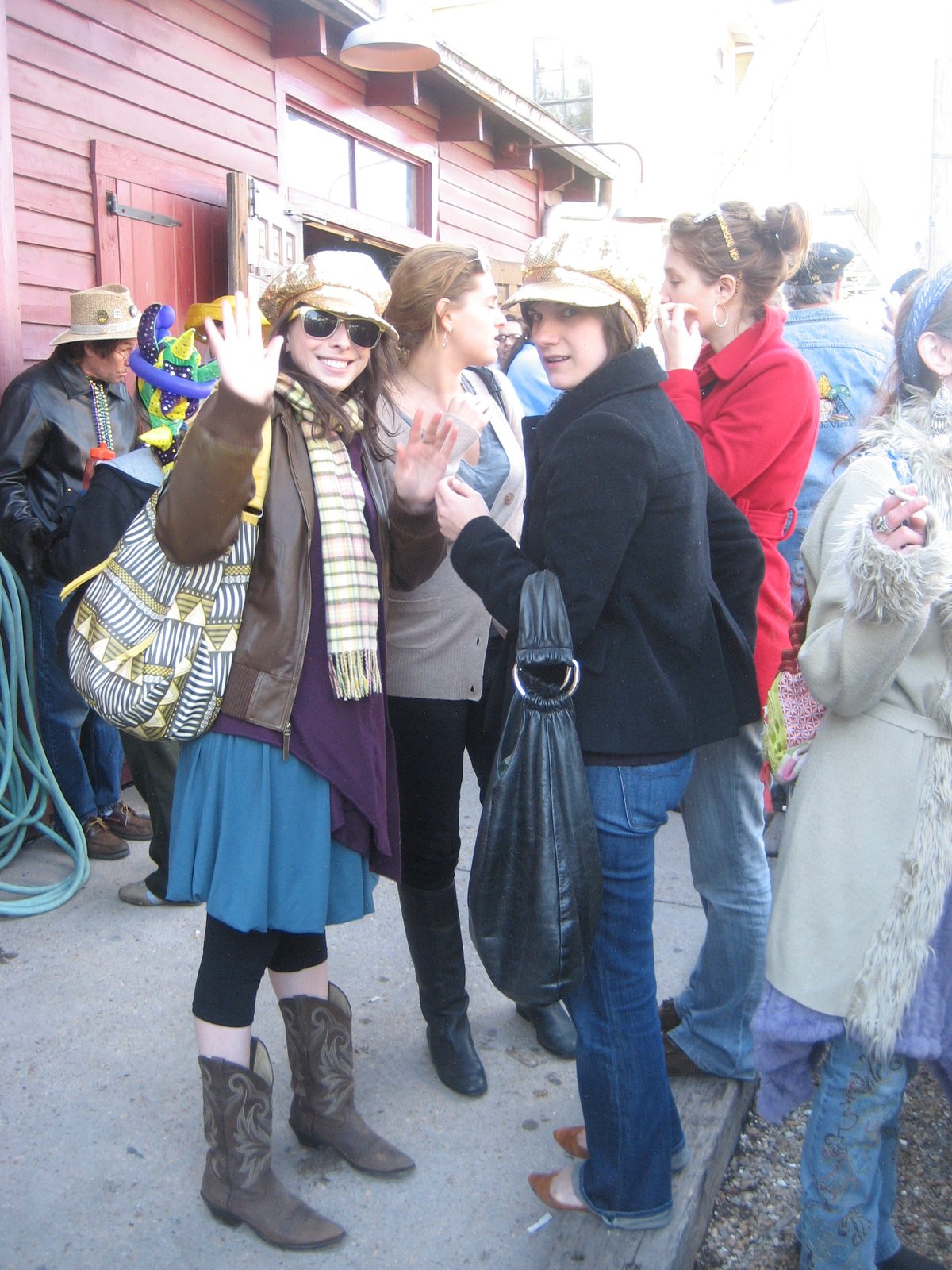 woman wearing brown cowboy boots with a blue skirt, dark capri leggings, brown leather jacket and gold cap at an outdoor event