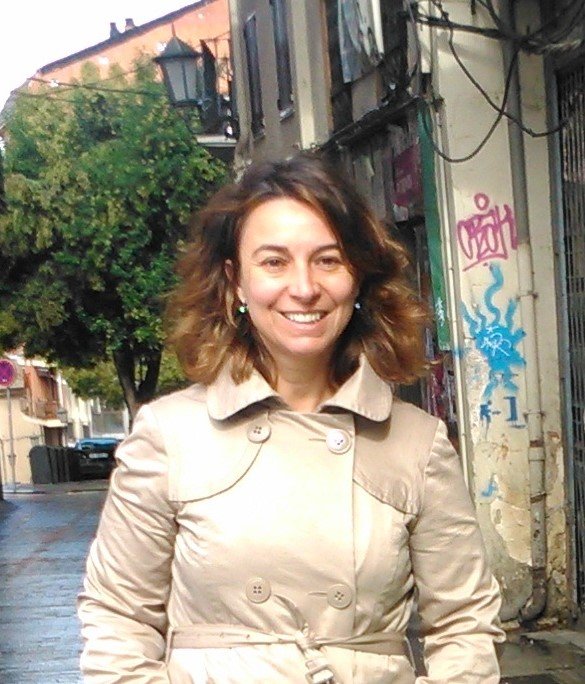 Woman on a city street smiling, wearing a light cream double-breasted belted trench coat