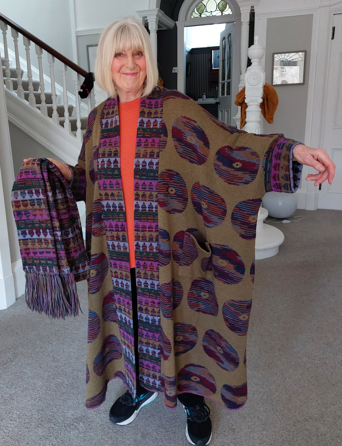 Woman wearing a colorful vintage Bill Gibb knit coat holding a matching fringed scarf