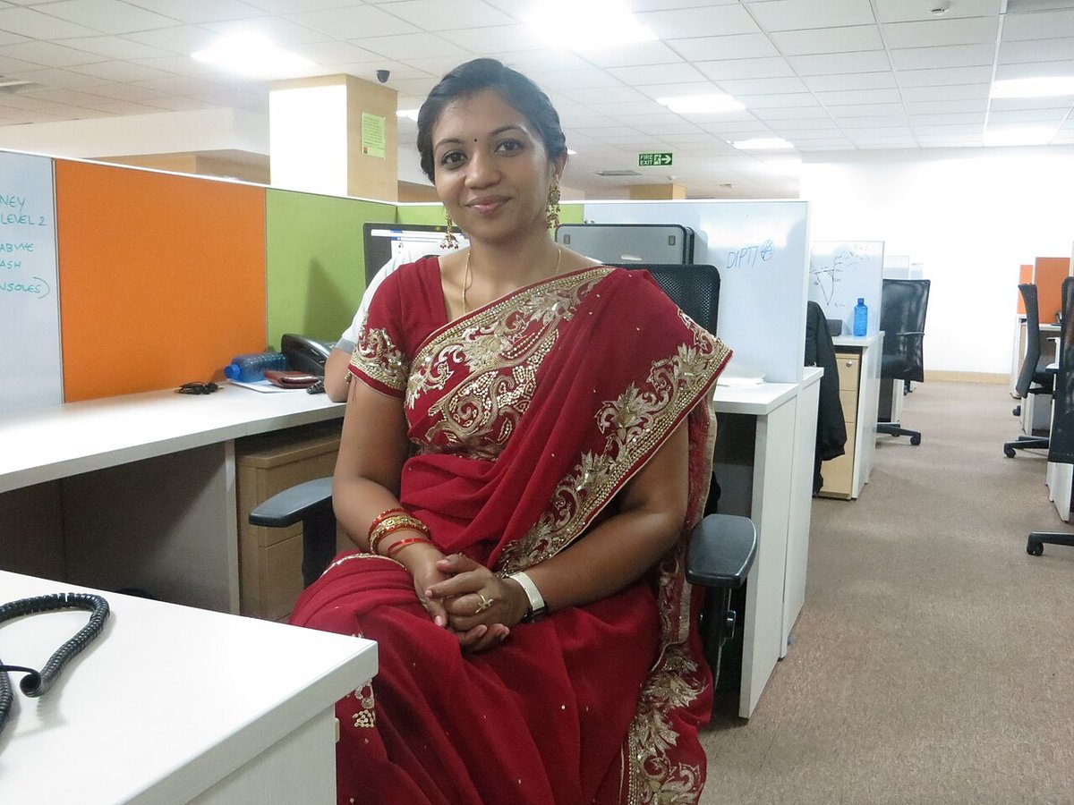 Woman seated in an office wearing a maroon-red silk saree with a wide gold embroidered border