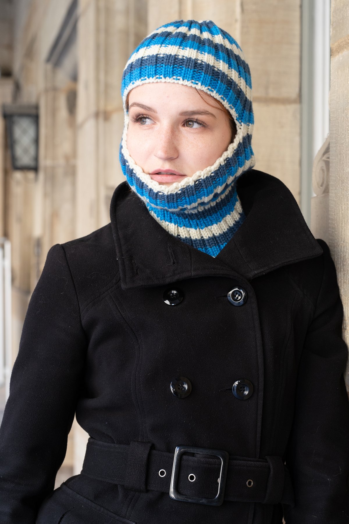 Woman wearing a blue and white striped knit balaclava with a black belted coat