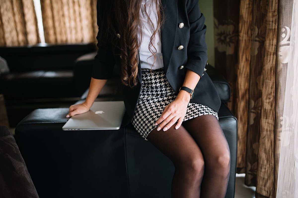 Seated woman in a black blazer, white shirt and houndstooth mini skirt with dark tights
