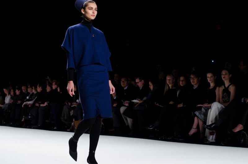 Model on the Carolina Herrera Fall/Winter 2014 runway wearing a cobalt-blue cape-style jacket and matching cobalt-blue pencil skirt with black tights and ankle boots.