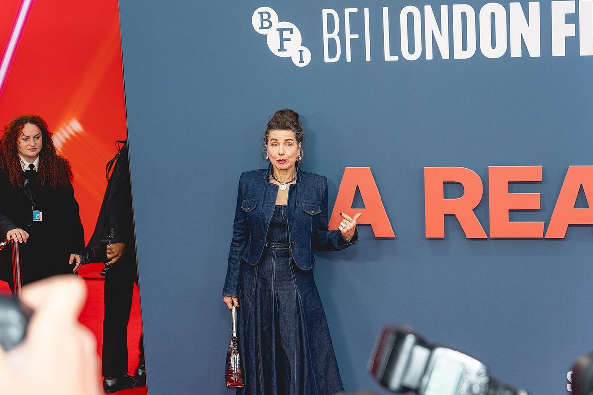 Woman posing at an evening event wearing a dark denim jacket over a long dark denim skirt with a small handbag