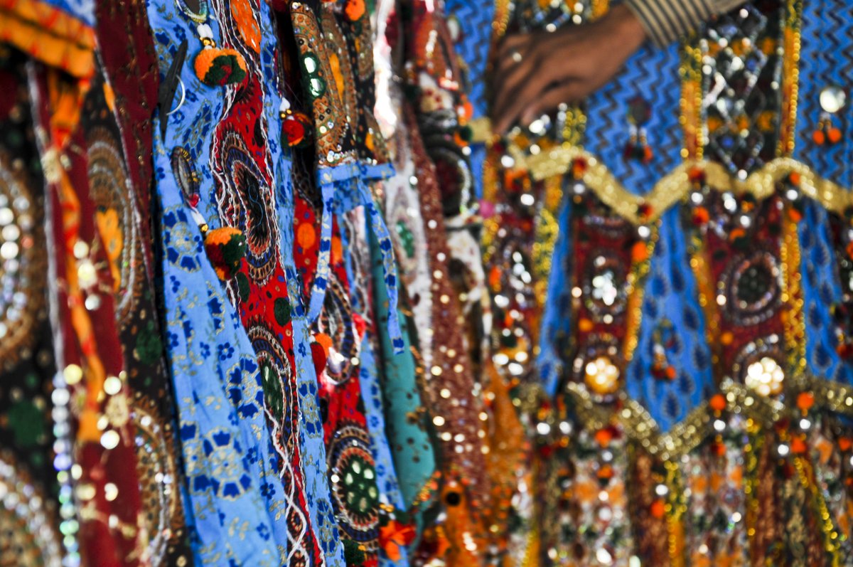 Close-up of colorful mirror-work chaniya choli skirts with embroidery and tassels at a market