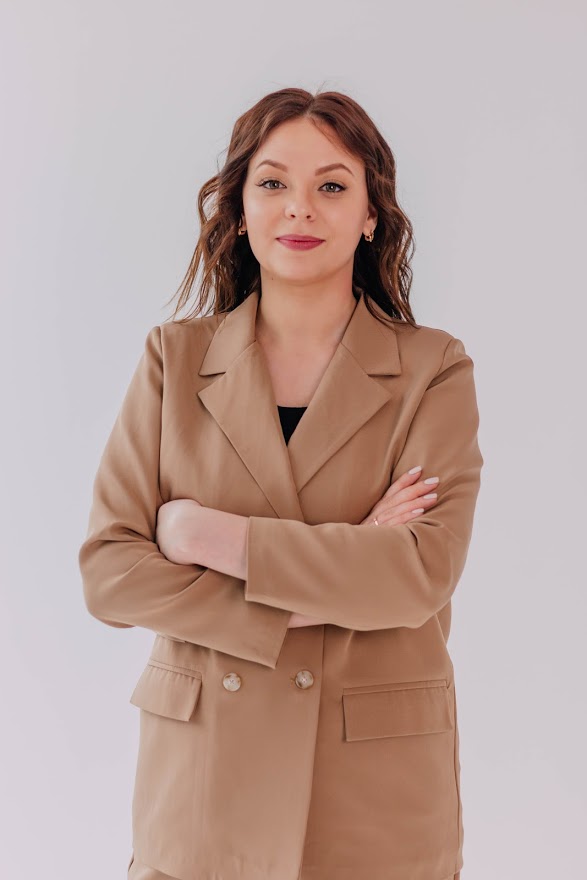 Studio portrait of a woman with arms crossed wearing a tan tailored blazer