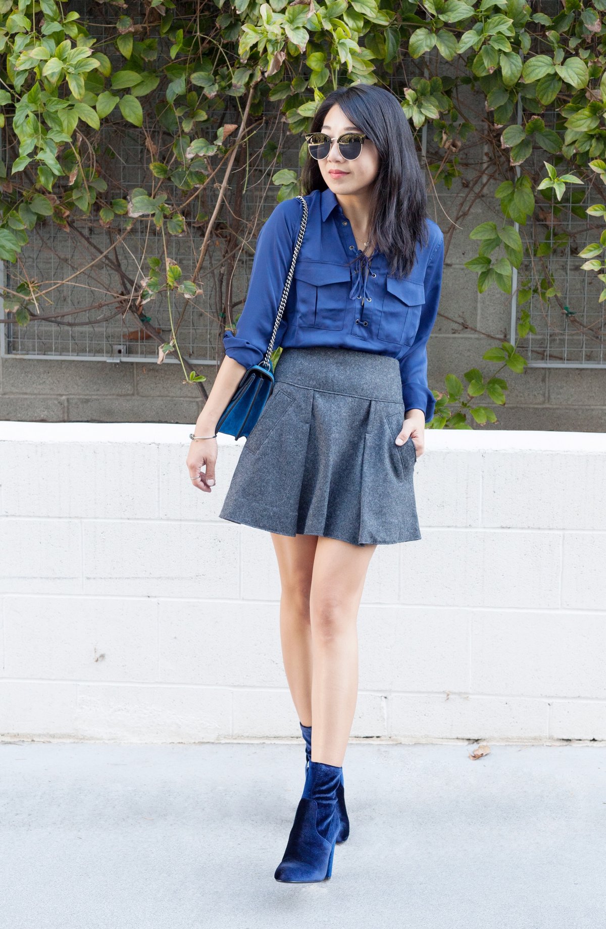 Woman wearing cobalt-blue velvet ankle boots with a royal-blue satin blouse and grey wool mini skirt.