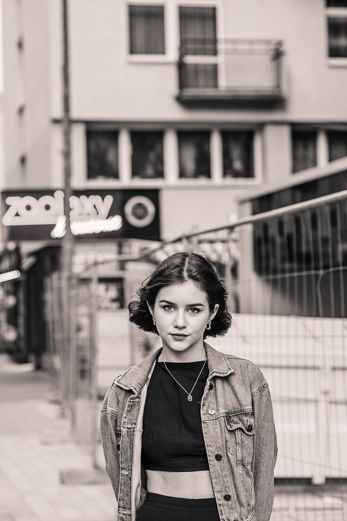 Black-and-white street portrait of a woman wearing a denim jacket over a dark top