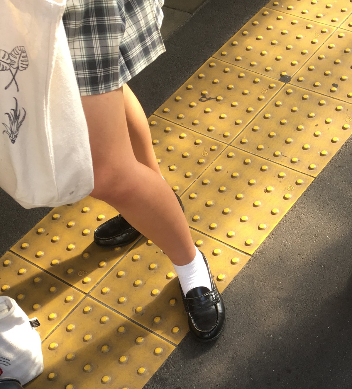 Close-up of a woman's legs in a grey and white plaid mini skirt, white ankle socks and black penny loafers on a Tokyo sidewalk
