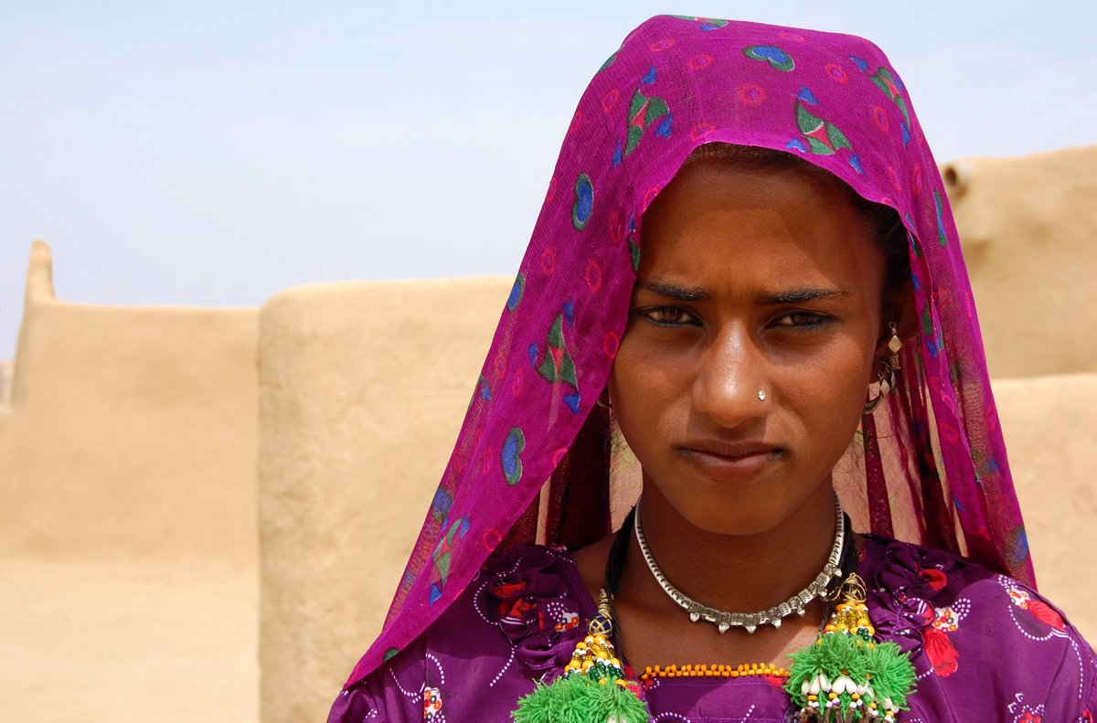 Woman in the Thar desert wearing a magenta printed headscarf with traditional jewellery.