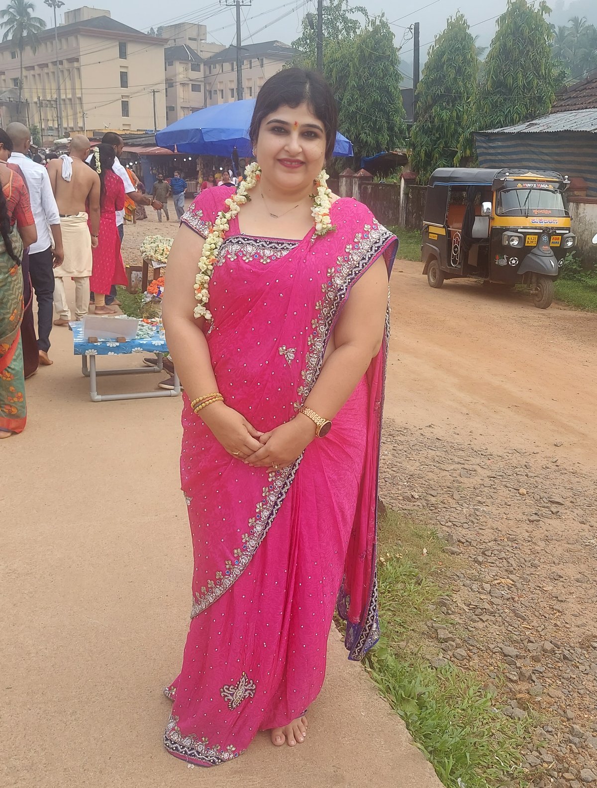 Woman in a bright pink saree with stone-work border and embellished blouse wearing a flower garland outdoors