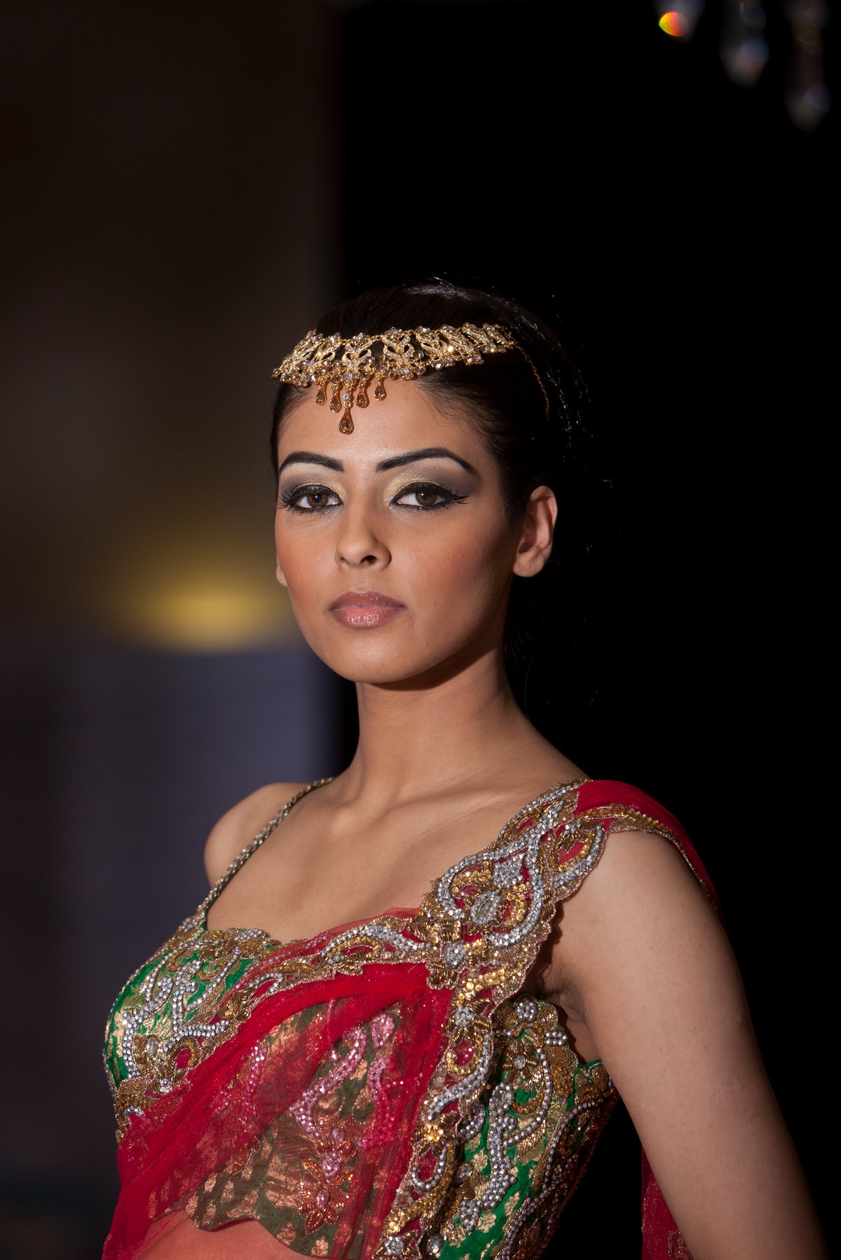 Woman wearing an embroidered red and green lehenga choli with a gold maang tikka on a runway