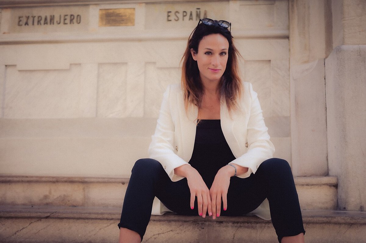 Woman in a white blazer over a black top and black cropped pants sitting on stone steps