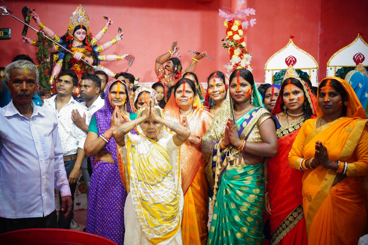 Group of women in colourful sarees in green, orange, yellow, purple and red standing with folded hands inside a temple during Dussehra