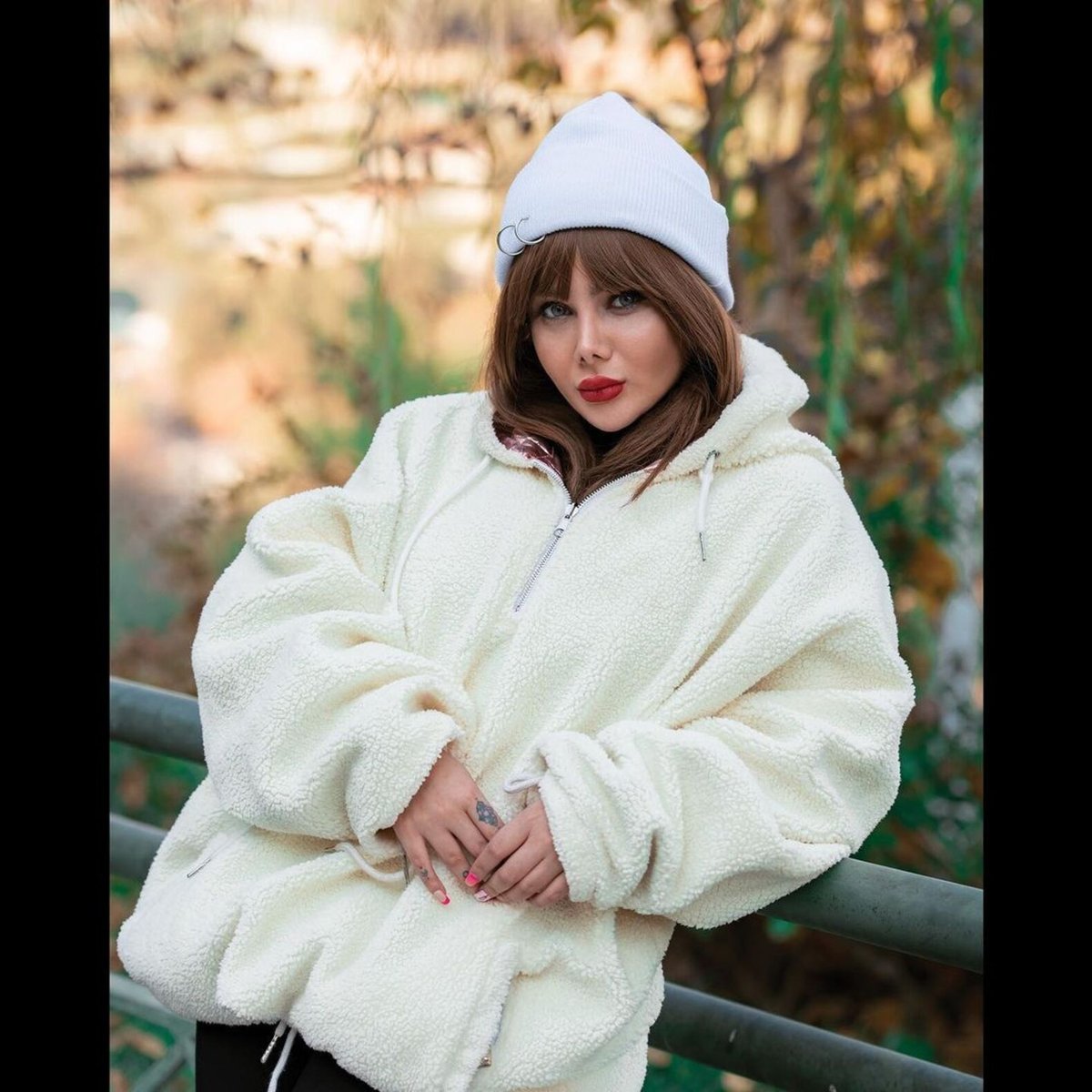 Woman in an oversized cream teddy-fleece half-zip pullover and a white knit beanie
