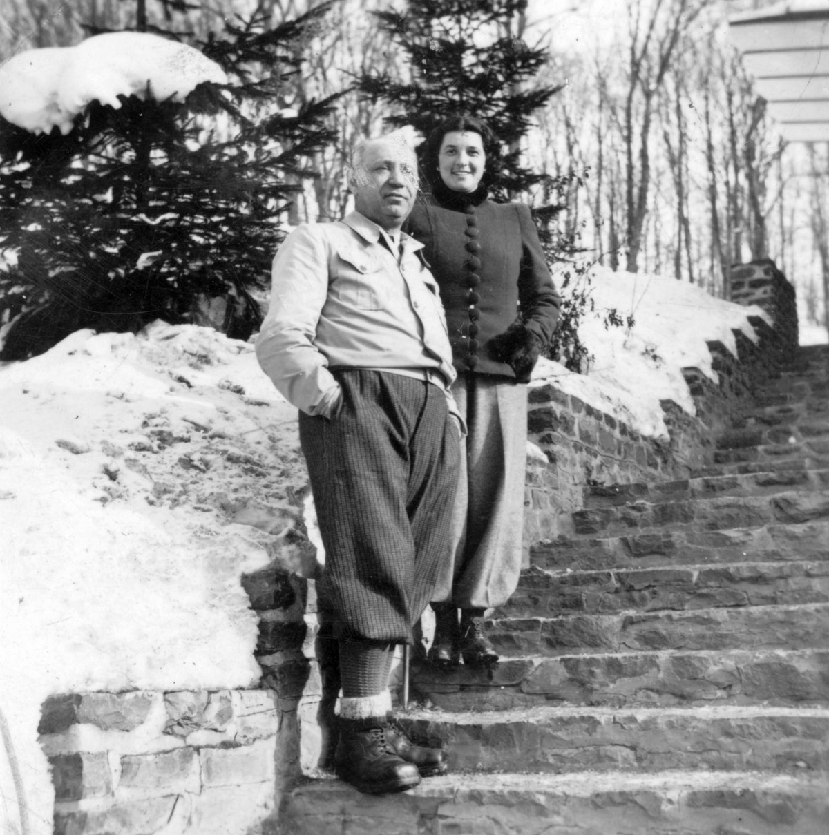 vintage black-and-white photograph of a couple standing on snowy stone steps, both wearing lace-up winter boots