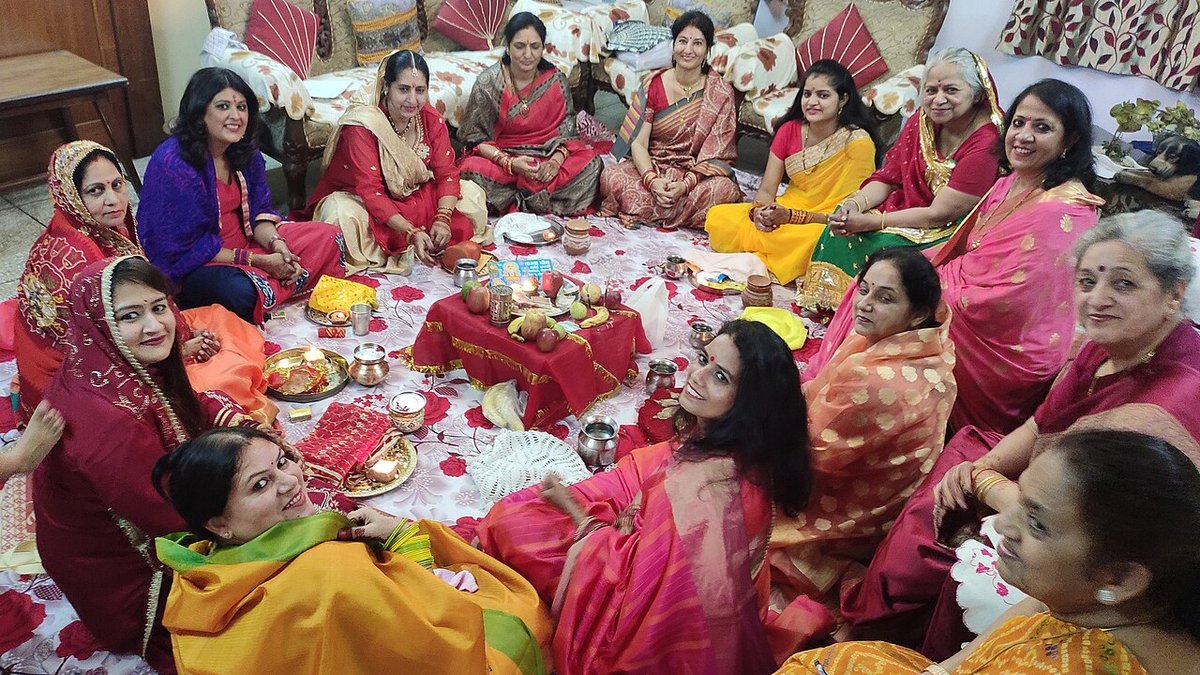 Group of women in colourful sarees in pink, red, yellow and green sitting in a circle with puja thalis for the Karva Chauth katha
