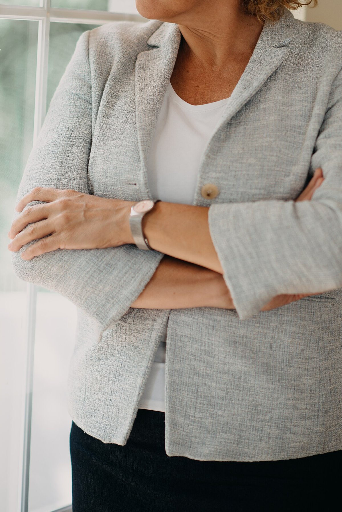 Woman in a gray blazer and white top standing with arms crossed in an office