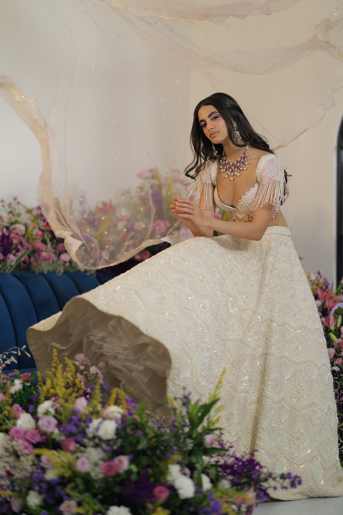 Woman in an ivory-white embroidered designer lehenga with a bead-fringed pink choli and statement jewelry
