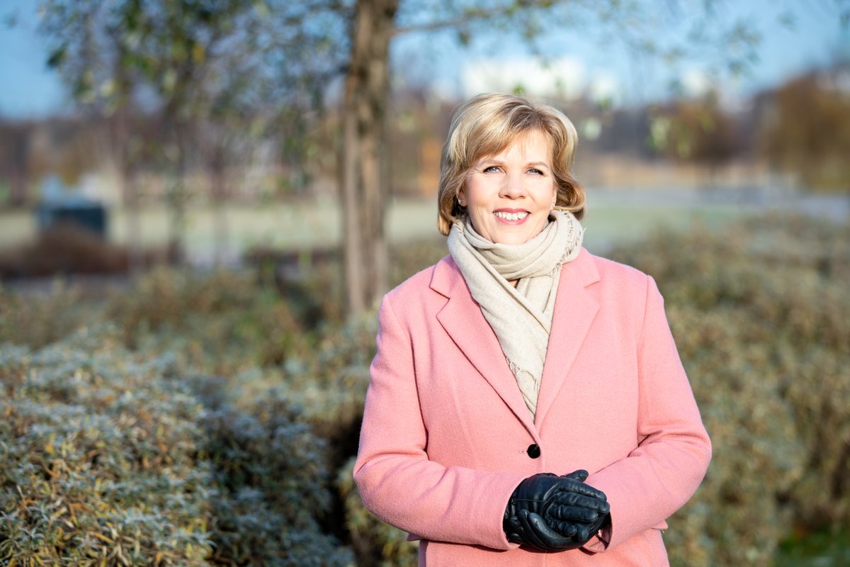 Smiling woman in a pink winter coat and cream scarf wearing black leather gloves