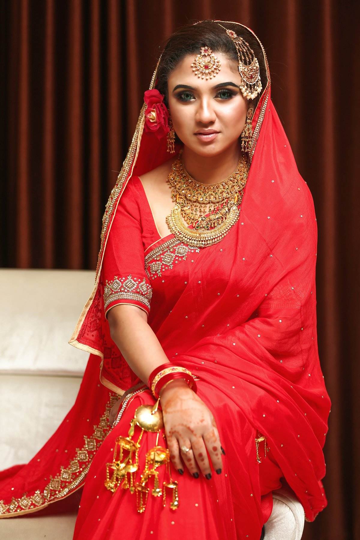 Woman in a red bridal-style lehenga with heavy gold jewelry, maang tikka, and red dupatta