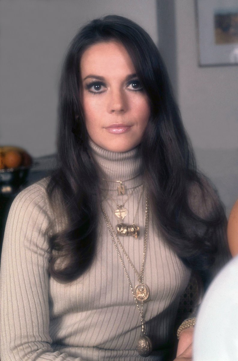 Woman wearing a cream ribbed turtleneck with multiple layered gold necklaces