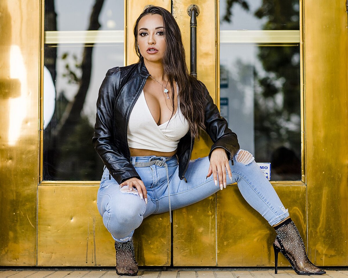 Woman seated on a doorstep wearing a black leather jacket over a white top with ripped light-blue jeans and heeled ankle boots
