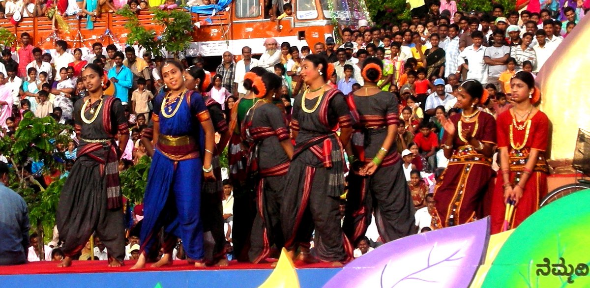 Women folk performers in black, blue and maroon traditional Karnataka dress with gold jewellery standing on a float at the Mysore Dasara procession