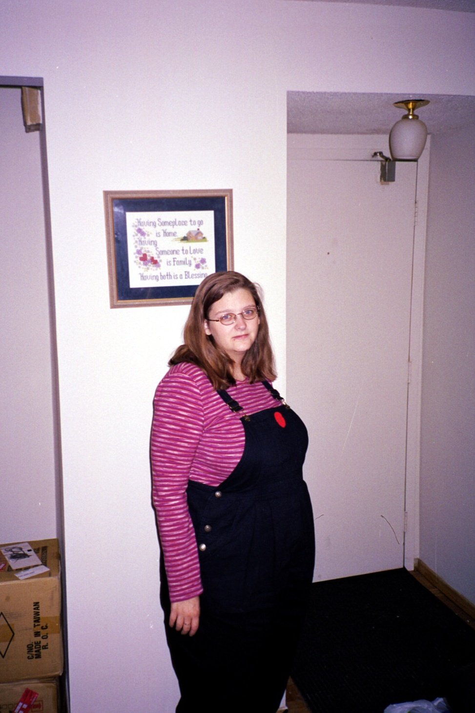 Woman standing indoors wearing black denim overalls over a pink striped long-sleeve top