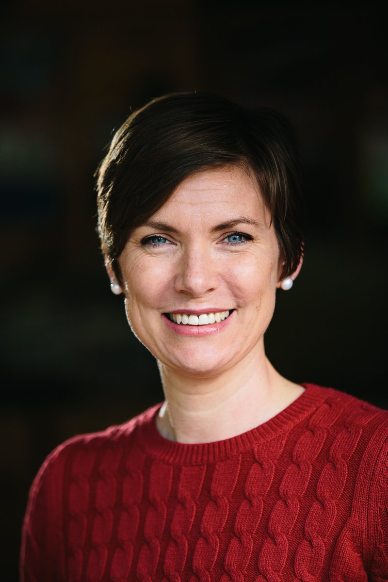 Smiling woman with short brown hair and pearl earrings in a head-and-shoulders portrait, wearing a wine-burgundy cable-knit crew-neck sweater