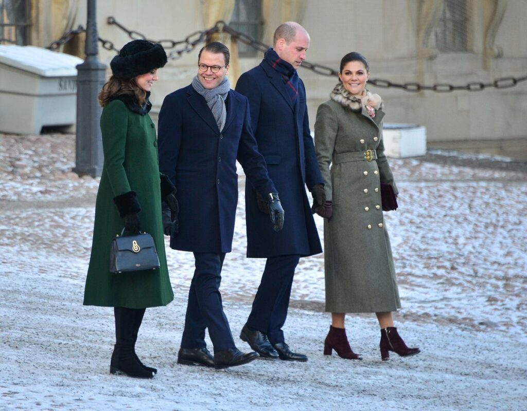 Kate Middleton in an emerald green coat and fur hat walking with Prince William and Swedish royals in a snowy courtyard, Crown Princess Victoria wearing a grey-olive double-breasted coat
