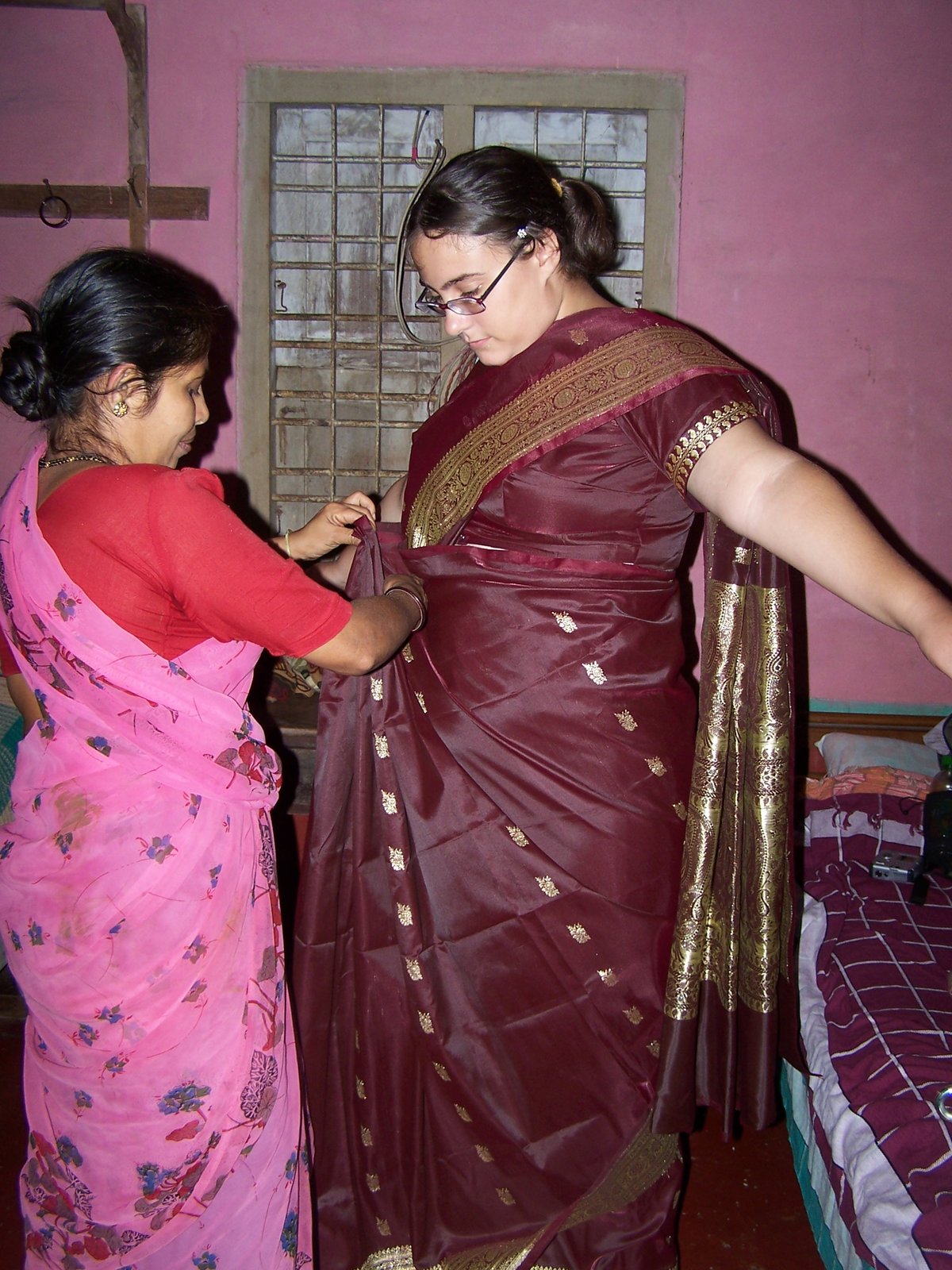 Woman helping another drape a maroon silk saree with a gold zari border