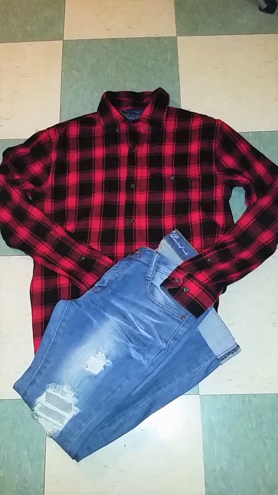 Flat lay of a red and black buffalo plaid flannel shirt with light-wash ripped jeans on a checkered tile floor