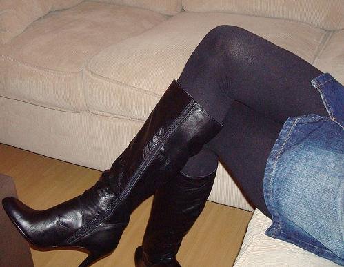 Black knee-high leather boots worn with black tights and a denim mini skirt.