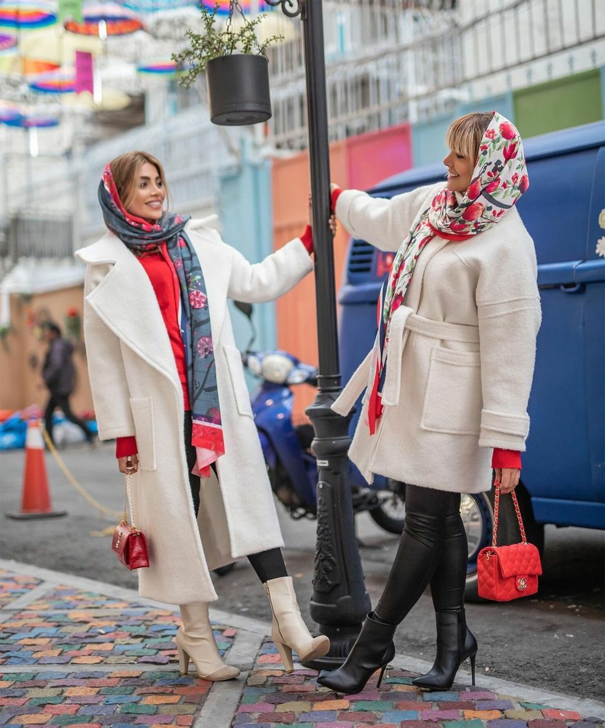 two women in cream wool coats on a city street, one wearing white heeled ankle boots and the other black heeled ankle boots