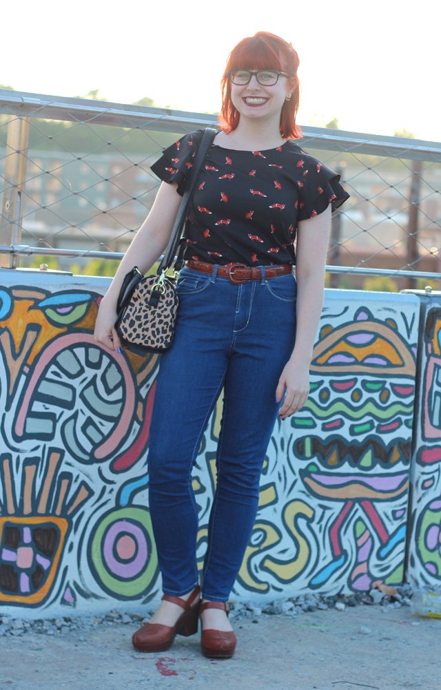 A woman wearing a black fox-print shirt and blue jeans, carrying a leopard print purse at her hip.
