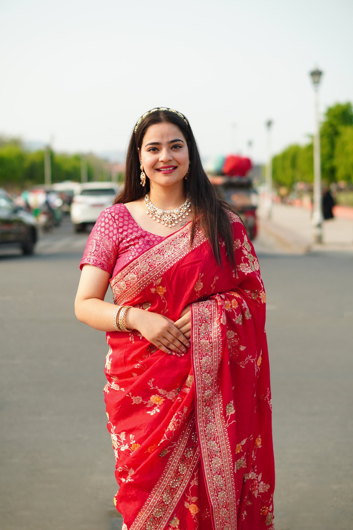 Woman in a red floral-printed saree with brocade border and pink brocade blouse standing outdoors