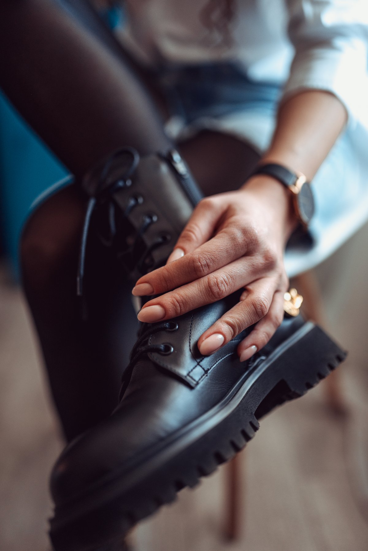 close-up of a woman adjusting black lace-up boots with chunky tread soles while wearing dark tights