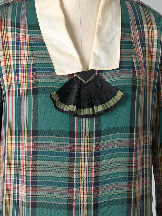 Museum mannequin close-up of a 1926 Jean Patou green plaid silk day dress with a cream collar and black pleated jabot