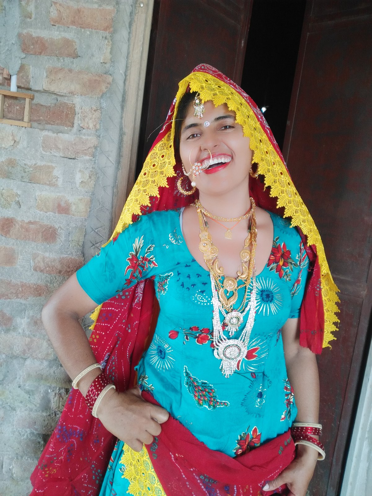 Woman in a turquoise floral kurta with a red and yellow bandhani odhni and layered gold jewelry