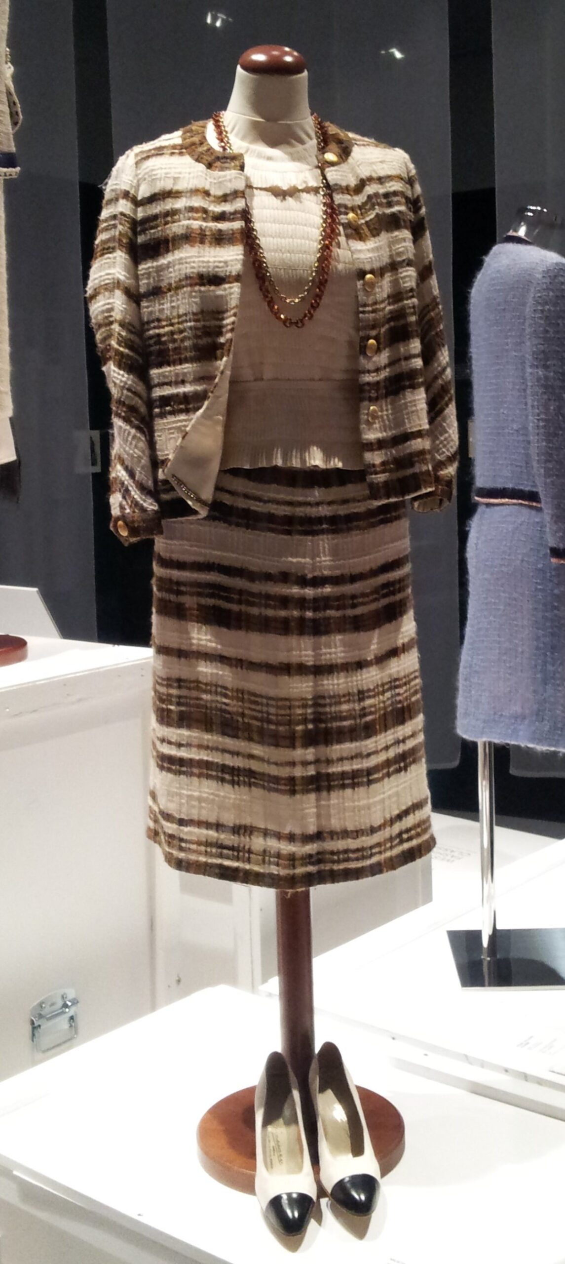 Museum mannequin displaying a 1965 Chanel brown and cream striped wool boucle tweed jacket with a matching skirt and silk blouse.