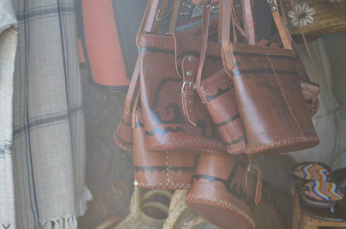 Several handcrafted brown leather handbags with dark decorative stitching hanging in a row at an artisan market stall