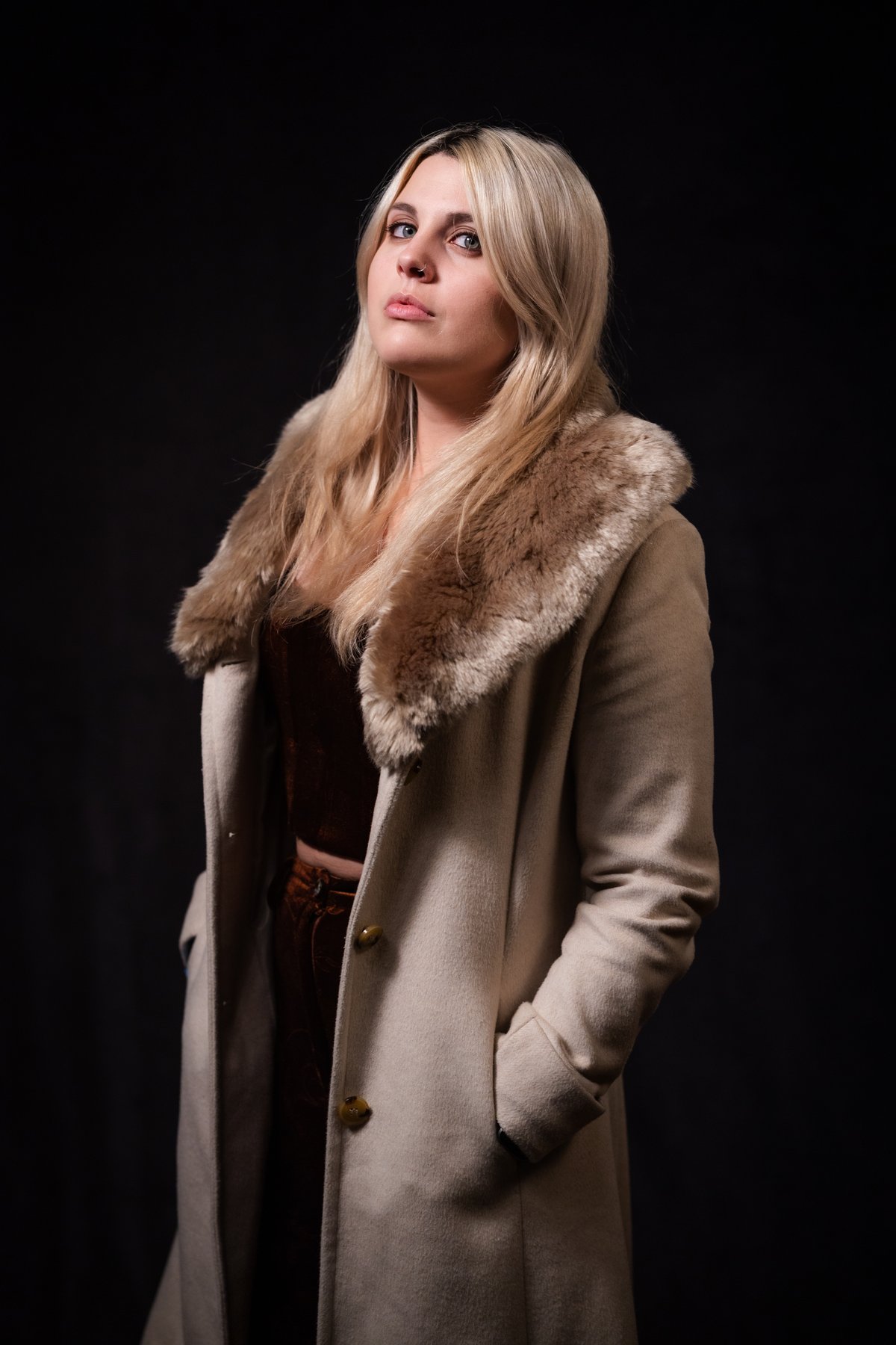 Woman wearing a beige wool coat with a fur collar over a brown velvet top