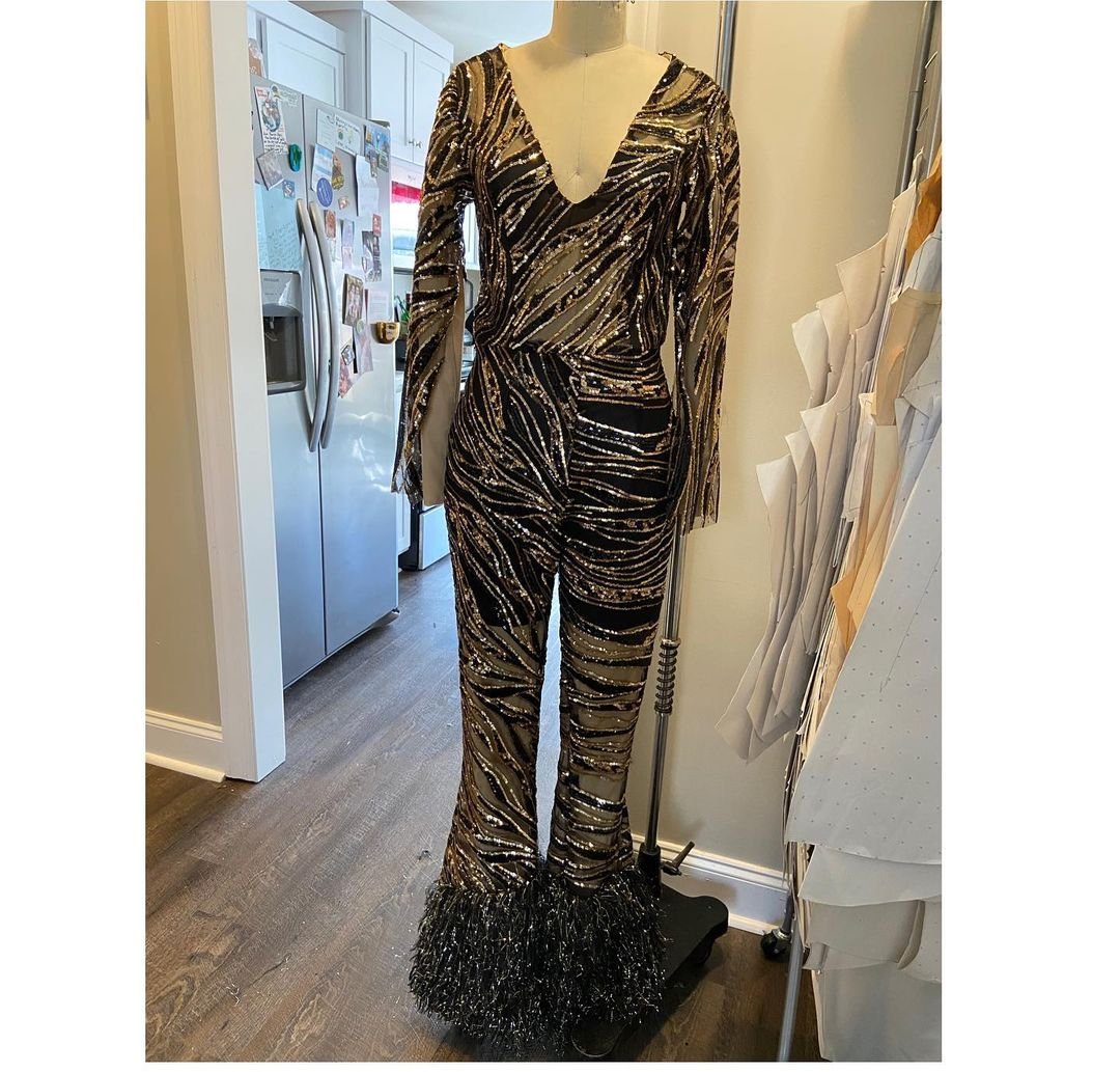 A black and gold sequined jumpsuit with fringe-trimmed flared legs displayed on a dress form
